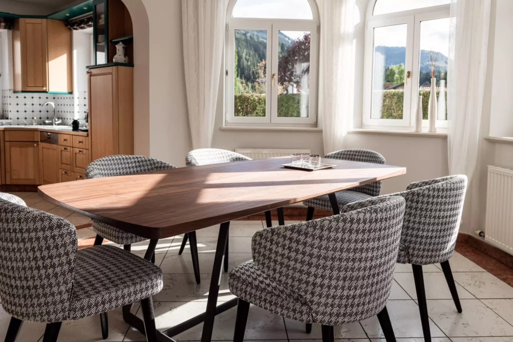 Esszimmer mit Minotti Designermöbeln, maßgefertigtem Holztisch und gepolsterten Stühlen vor großen Fenstern mit weißen