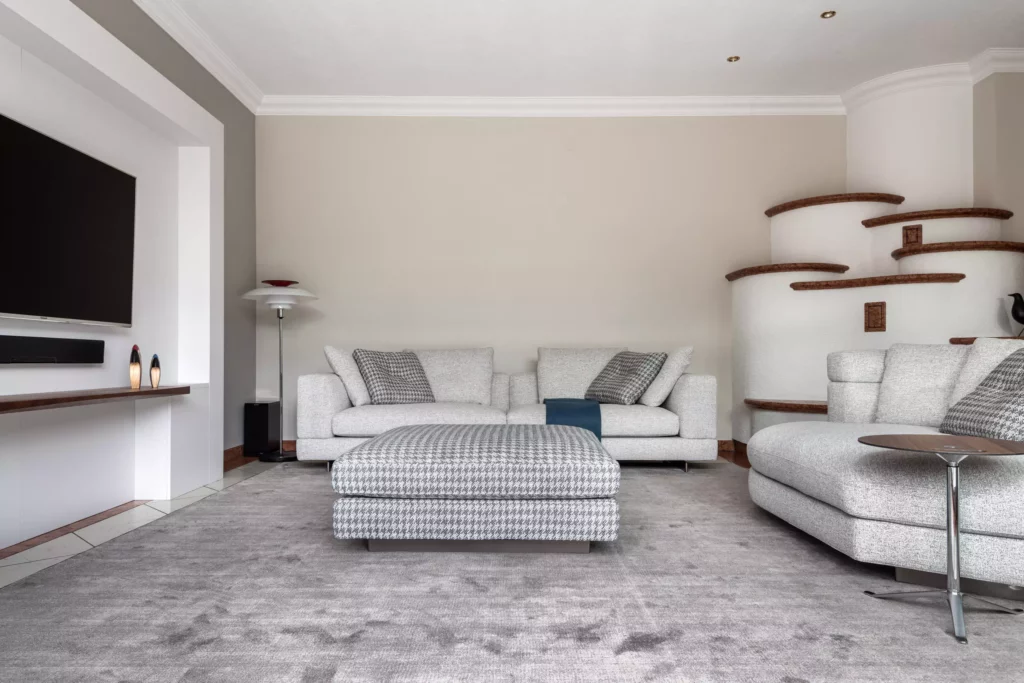 Modernes Wohnzimmer mit hellgrauem Minotti Sofa, gemustertem Hocker, grauem Teppich und integrierter Wohnraumplanung in