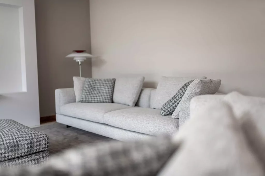 Helles Wohnzimmer mit grauem Minotti-Sofa, gemusterten Kissen, Teppich und moderner Stehlampe als Innenarchitektur-Raumlösung