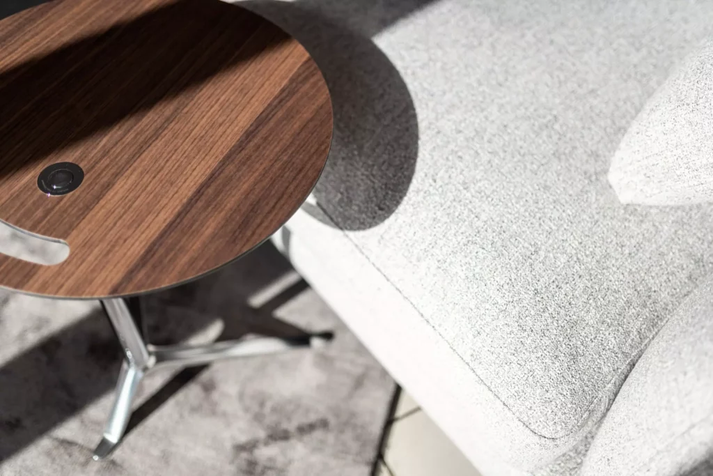 Runder Minotti Beistelltisch mit Holzplatte und Metallfuß neben hellgrauem Polstermöbel im Showroom für Innenarchitektur und