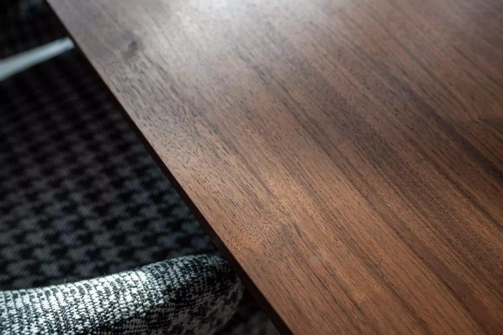 Nahaufnahme einer Tischplatte aus dunklem Holz und eines gepolsterten Stuhlbezugs mit schwarz-weißem Muster im Minotti