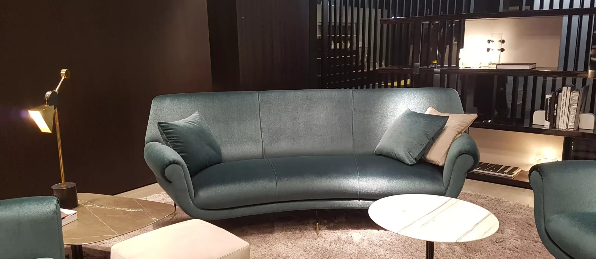 Wohnzimmer-Showroom mit Minotti Sofa in Petrol, beigem Hocker, zwei Beistelltischen und Teppich, moderne Innenarchitektur in