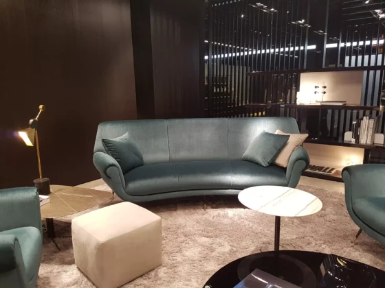 Wohnzimmer-Showroom mit Minotti Sofa in Petrol, beigem Hocker, zwei Beistelltischen und Teppich, moderne Innenarchitektur in