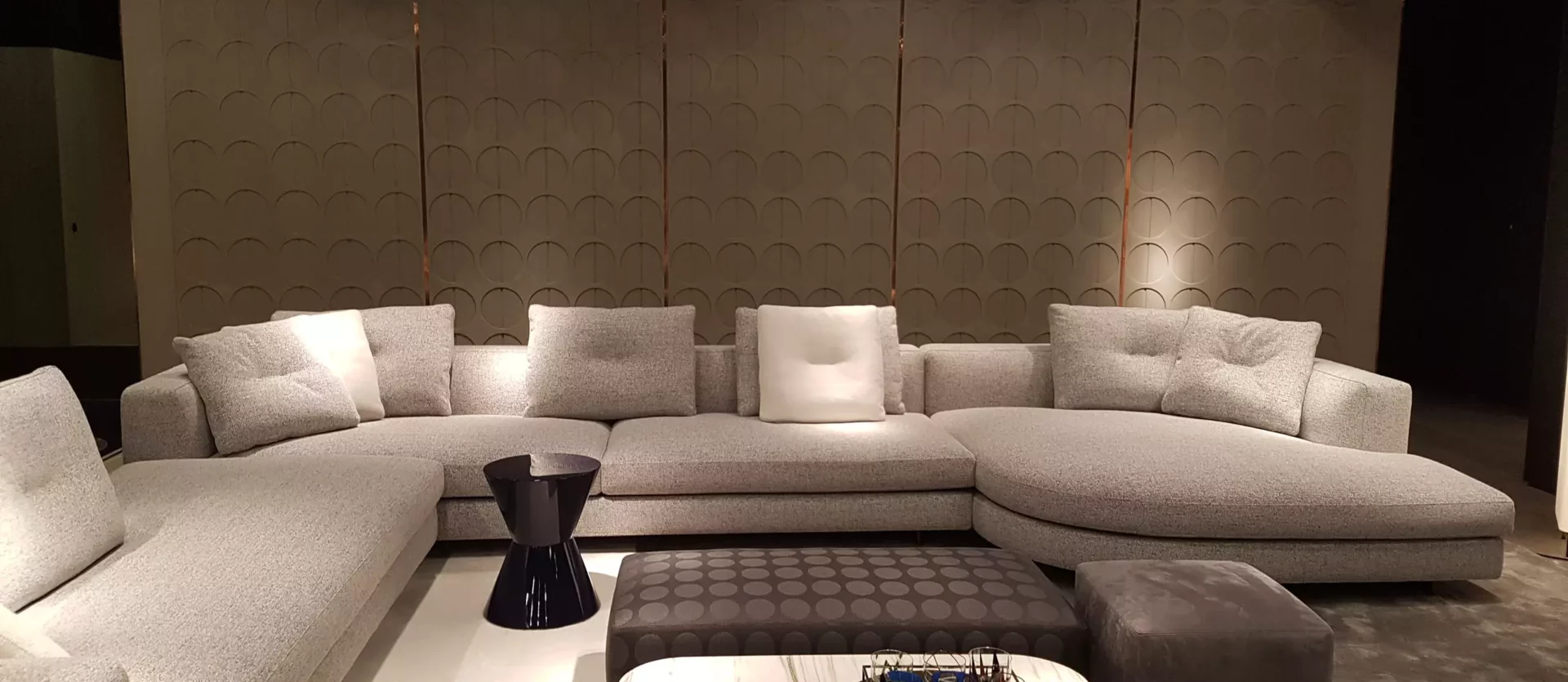 Moderner Minotti Wohnbereich mit grauem Ecksofa, Beistelltisch, gepolstertem Hocker und dekorativer Wand im Showroom Salzburg