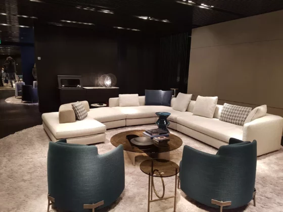 Modernes Wohnzimmer mit cremefarbenem Minotti Ecksofa, zwei blauen Sesseln, runden Glastischen und Teppich im Showroom