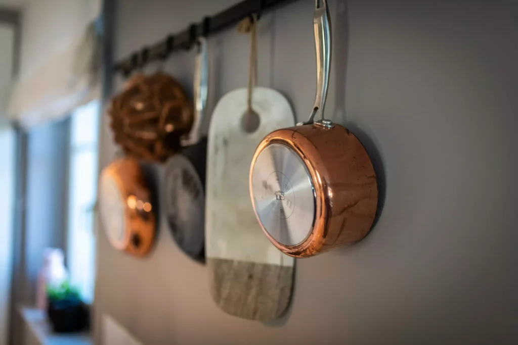 Kupferne Töpfe und Küchenutensilien hängen an einer Wand in einem modernen Wohnraum mit Innenarchitektur und maßgefertigter