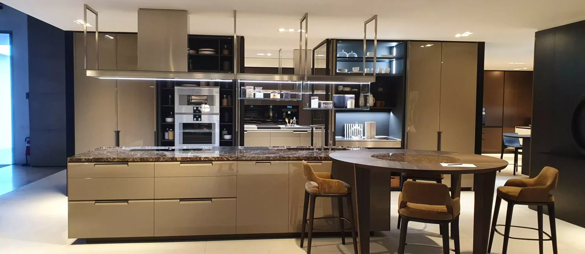 Moderne Poliform Küche mit Kochinsel, integriertem Ofen, Essbereich mit runder Holzplatte und vier Polstermöbeln im Showroom