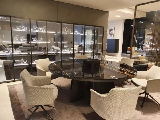 Moderner Poliform Essbereich mit rundem schwarzem Glastisch und sechs gepolsterten Stühlen vor beleuchtetem Vitrinenschrank