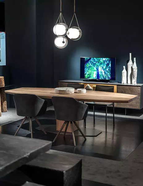 Moderner Riva1920 Massivholztisch mit zwei Stühlen in elegantem Möbelstudio mit dunkler Wand und Designbeleuchtung