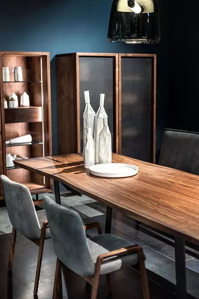 Massivholztisch von Riva1920 mit grauen Stühlen, dekorative Flaschen und Teller, modernes Möbelstudio mit Vitrinen und