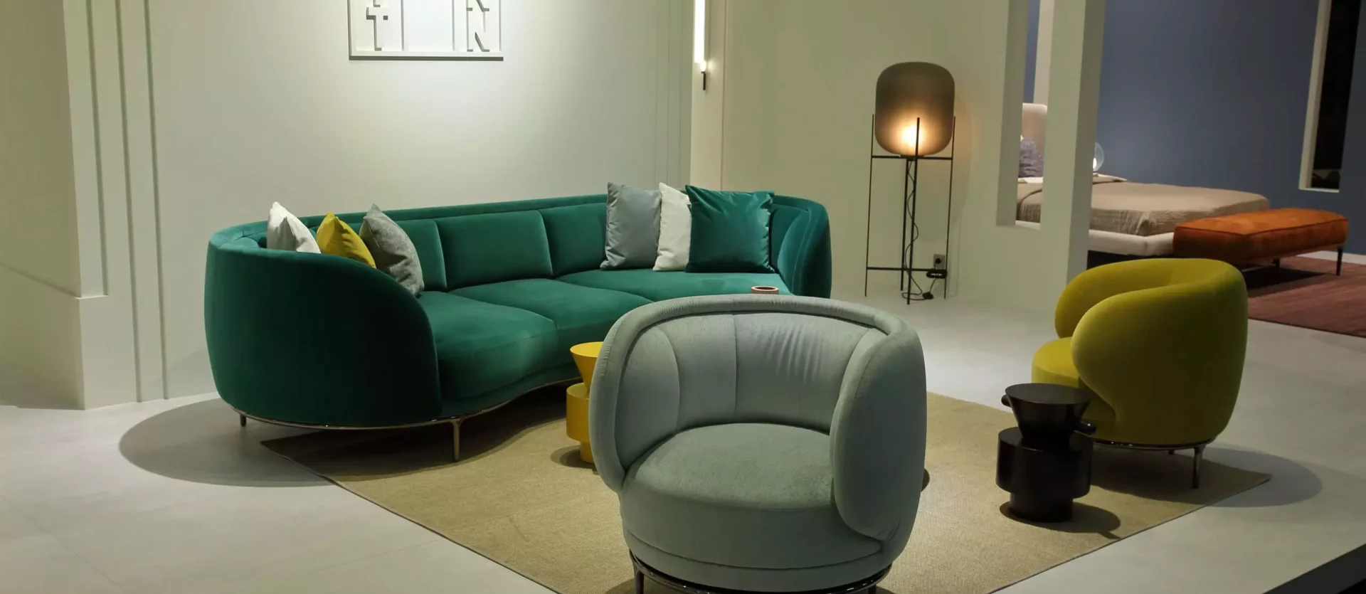 Modernes Wohnzimmer mit grünem Wittmann Sofa, zwei Sesseln in Hellgrün und Gelb, Teppich und Stehlampe im Möbelstudio