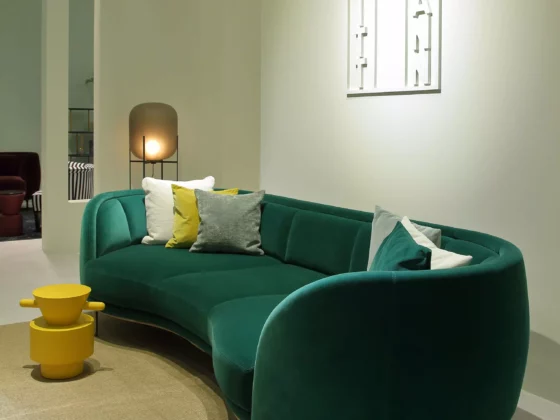 Grünes, geschwungenes Sofa mit bunten Kissen im modernen Showroom mit Wittmann Wanddeko und gelbem Beistelltisch