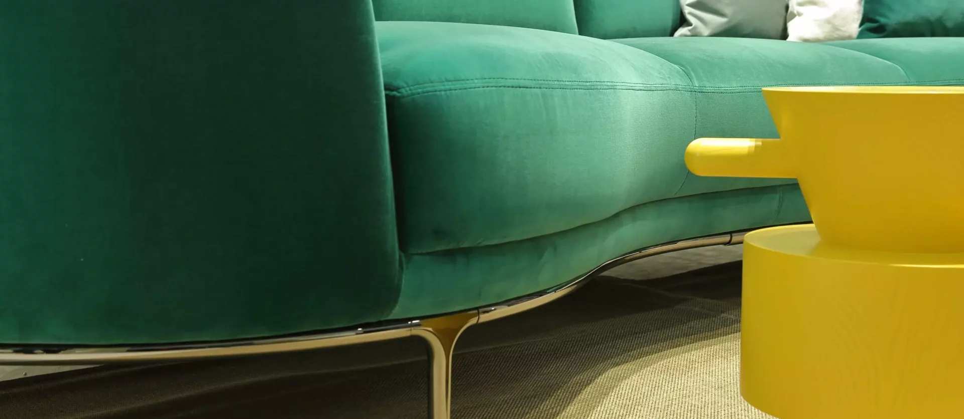 Grünes Wittmann Sofa mit Metallfüßen und gelbem Design-Beistelltisch auf Teppich im Möbelstudio Showroom