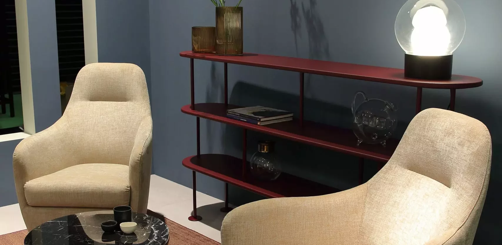 Gemütliche Sitzecke mit zwei beigen Polstersesseln, rundem Couchtisch mit schwarzer Marmorplatte und rotem Regal, Wittmann