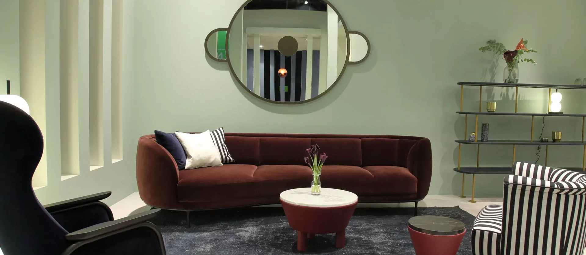 Modernes Wohnzimmer mit braunem Sofa, gestreiftem Sessel, blauem Sessel, runden Tischen und rundem Wandspiegel, Wittmann