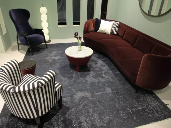 Wohnzimmer mit bordeauxrotem Wittmann Sofa, gestreiftem Sessel, dunkelblauem Sessel, runden Tischen und modernem Teppich im