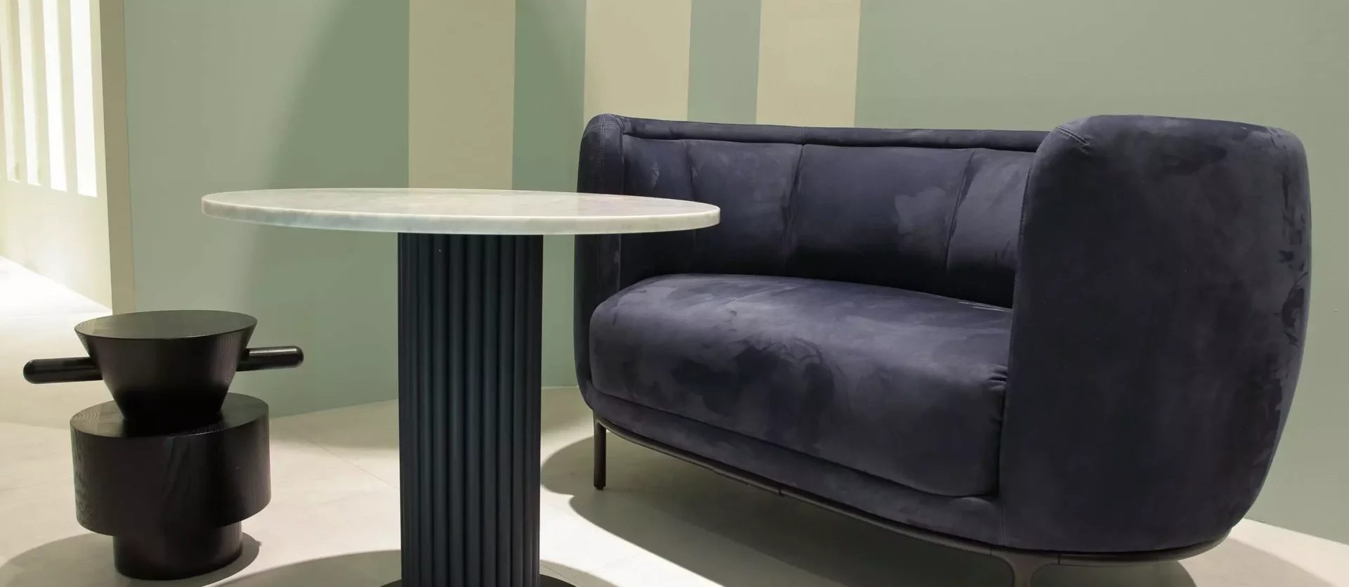 Dunkelblaues Sofa mit Samtbezug neben rundem Marmor-Tisch mit schwarzem Säulenfuß und skulpturalem Beistelltisch, Wittmann
