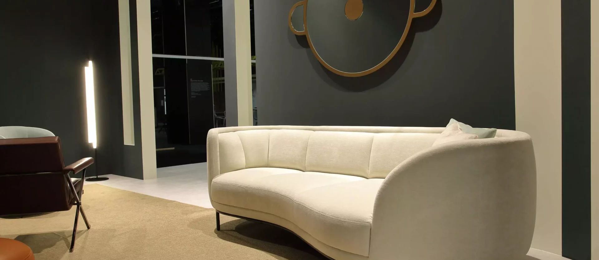 Beiges, geschwungenes Sofa aus der Wittmann Kollektion in modernem Showroom mit rundem Wandspiegel und Teppichboden