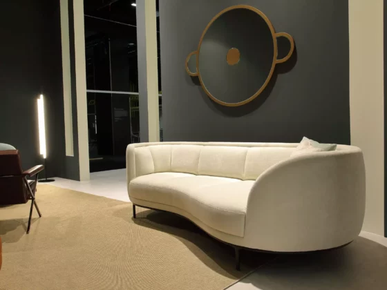 Beiges, geschwungenes Sofa aus der Wittmann Kollektion in modernem Showroom mit rundem Wandspiegel und Teppichboden