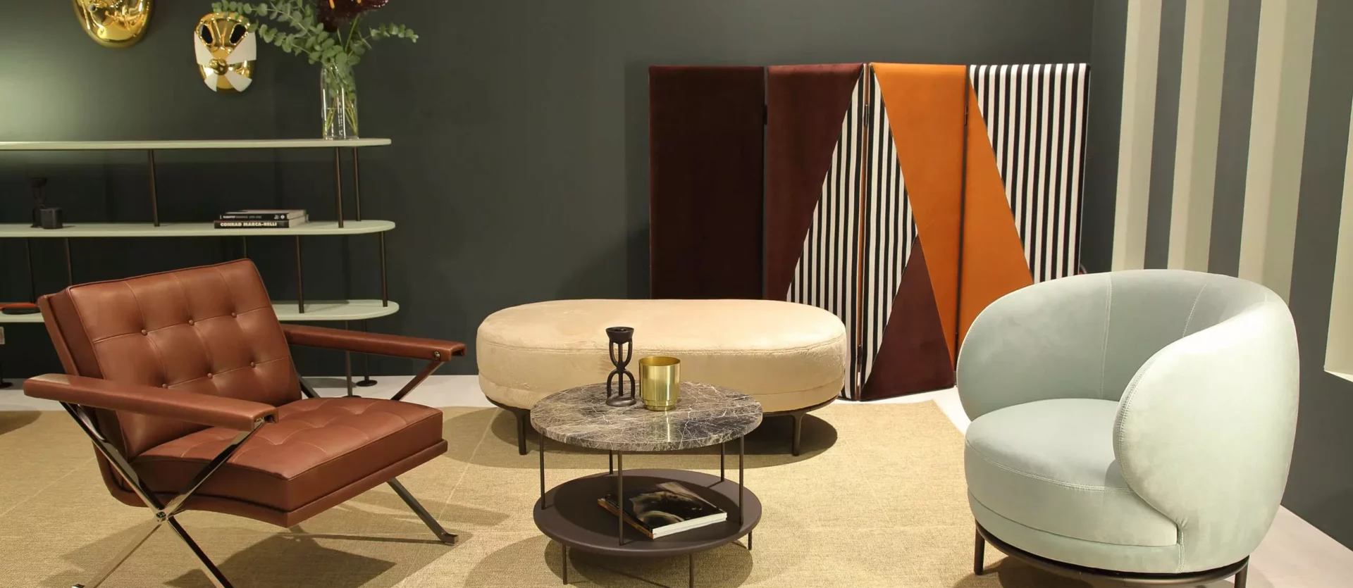 Modernes Wohnzimmer mit braunem Ledersessel, hellblauem Polstersessel, ovalem Hocker, rundem Couchtisch und, Wittmann