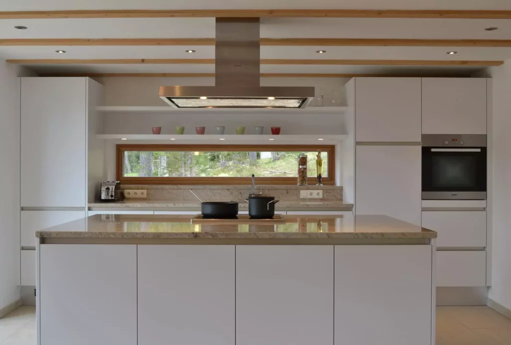 Moderne weiße Küche mit Kochinsel, Granitarbeitsplatte, Dunstabzug, Einbauofen und Fenster mit Blick ins Grüne, Referenzen