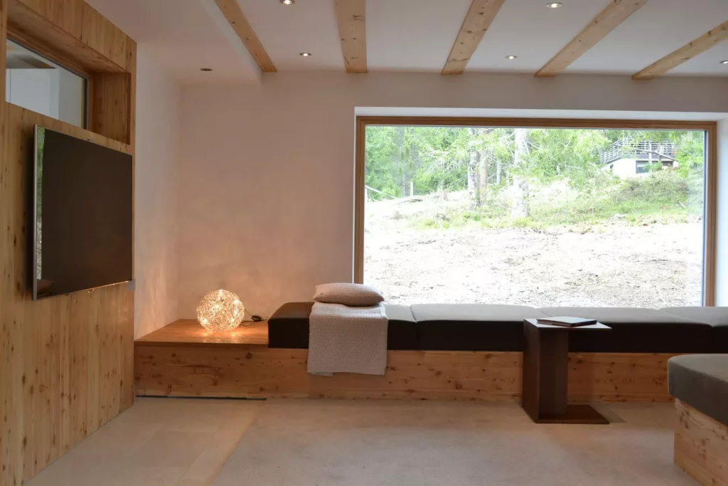 Modernes Ferienhaus-Wohnzimmer mit maßgefertigter Holzbank, großem Panoramafenster, indirekter Beleuchtung und, Referenzen