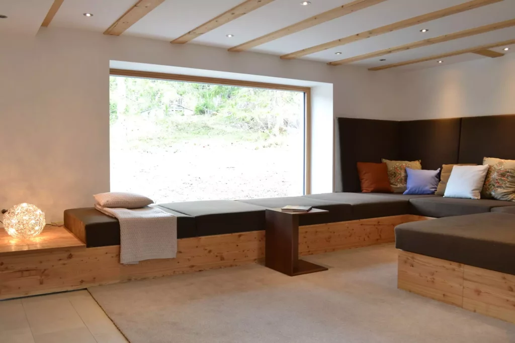 Modernes Ferienhaus-Wohnzimmer mit maßgefertigtem Holzsofa, bunten Kissen, großem Fenster und indirekter, Referenzen