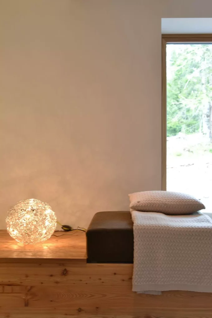 Gemütliche Sitzecke mit braunem Polster, hellbeiger Decke und Kissen auf Holzpodest neben leuchtender Kugellampe, Referenzen