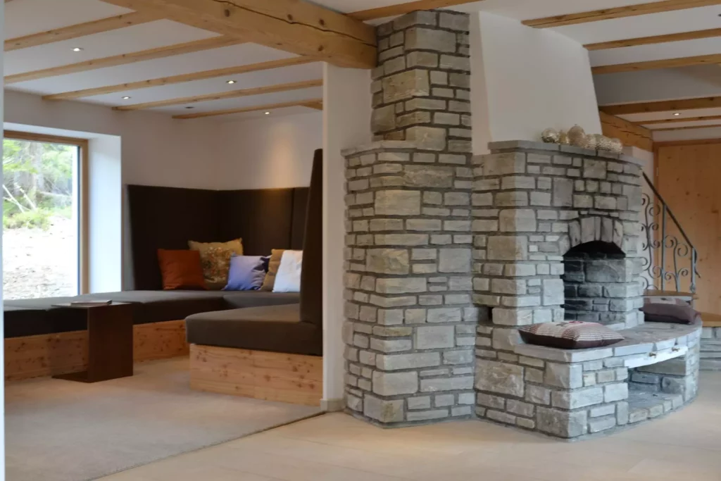 Gemütlicher Wohnbereich mit maßgefertigter Eckbank aus Holz und Polstern neben einem rustikalen Kamin aus, Referenzen