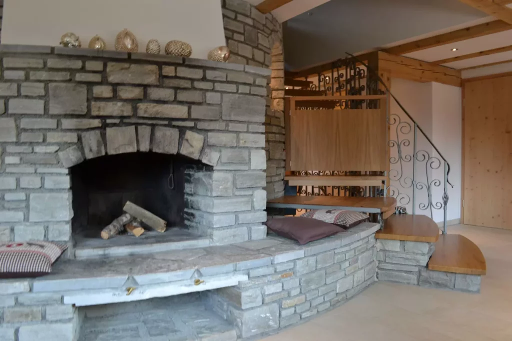 Gemauerter Kamin mit Holzscheiten und Sitzbank mit Kissen neben Holztreppe mit geschwungenem Metallgeländer in, Referenzen