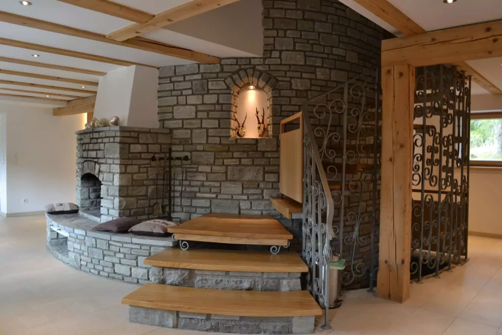 Wohnraum mit maßgefertigter Holztreppe und Sitzbank aus Stein vor Kamin in Ferienhaus Wagrain, Innenarchitektur, Referenzen