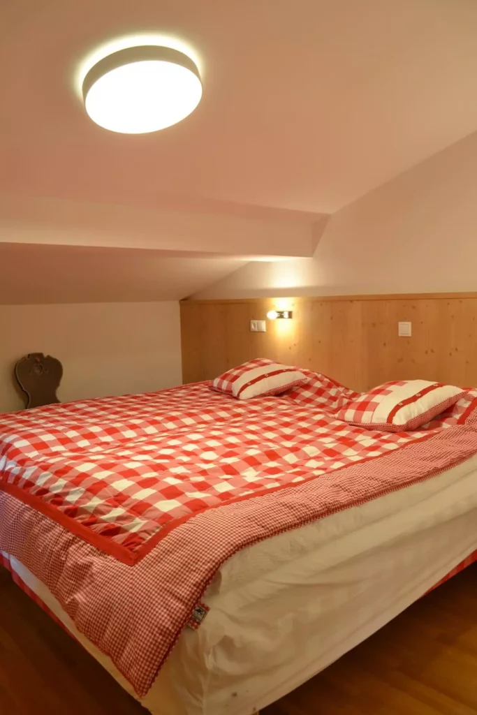 Schlafzimmer mit rotem kariertem Bettbezug, Holzwandverkleidung und moderner Deckenleuchte in Ferienhaus Wagrain, Referenzen
