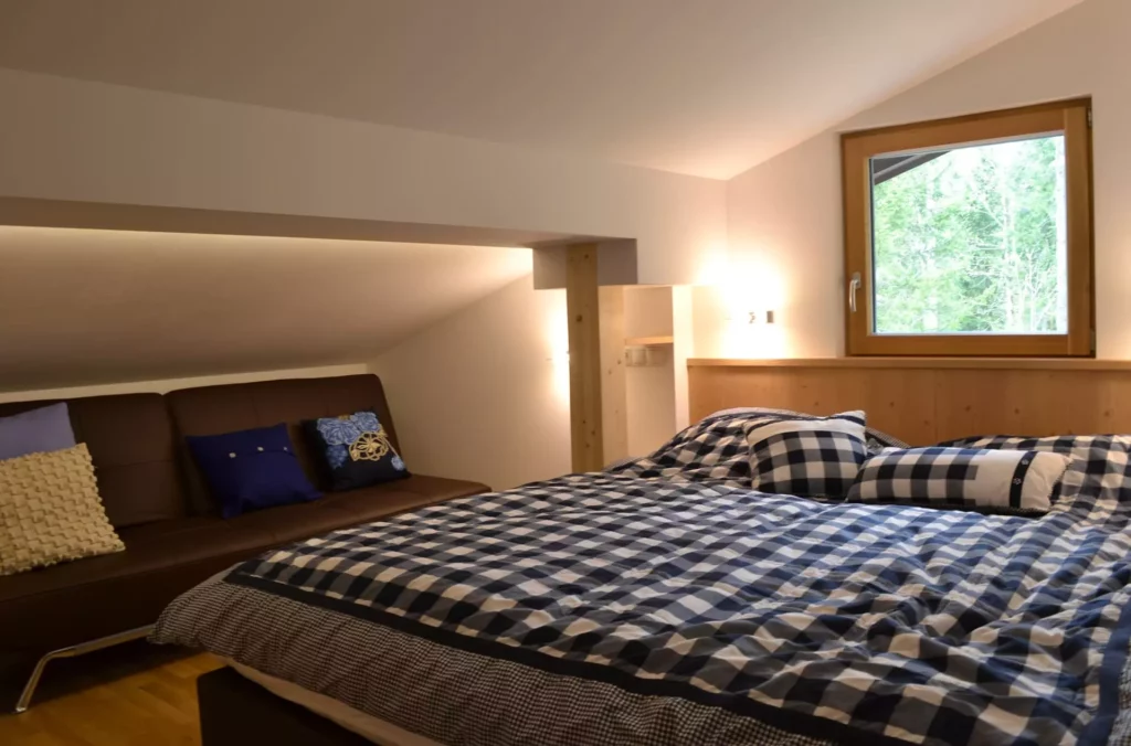 Schlafzimmer mit Dachschräge, maßgefertigtem Holzbett und Sofa, Fenster mit Blick auf Wald, Innenarchitektur, Referenzen
