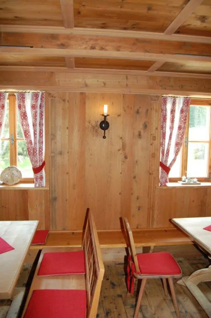 Rustikaler Gastraum mit Holzvertäfelung, Holzmöbeln mit roten Sitzpolstern, Fenstern mit rot-weiß gemusterten, Referenzen
