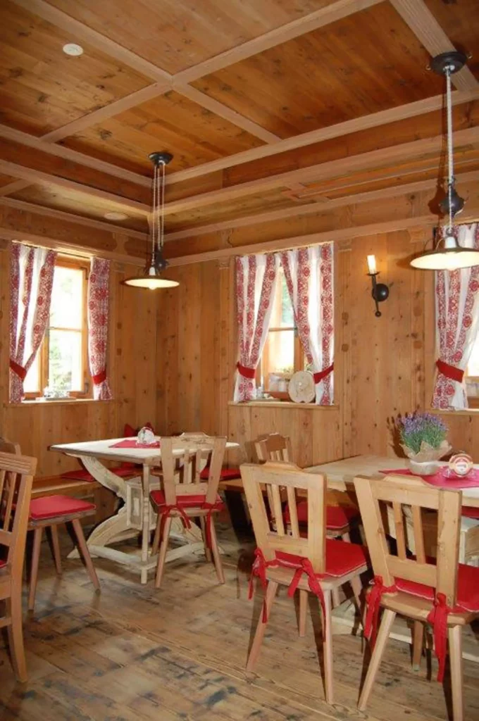 Gemütlicher Gastraum mit Holzvertäfelung, Holztischen und Stühlen mit roten Sitzkissen, dekorativen Vorhängen, Referenzen