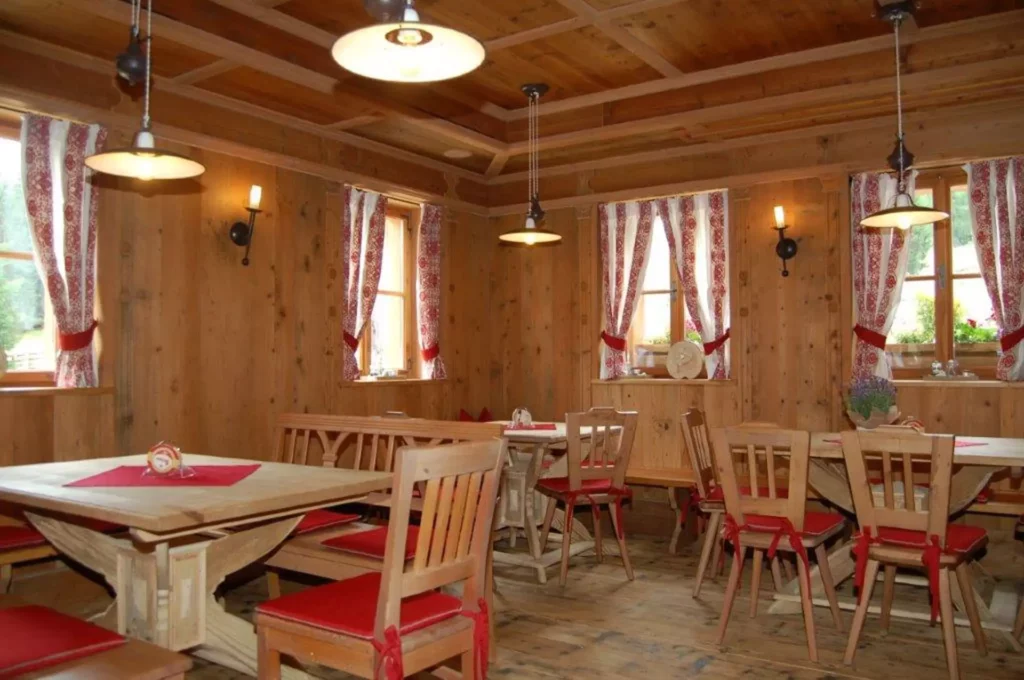 Rustikaler Gastraum mit maßgefertigten Holztischen und Stühlen mit roten Sitzkissen, Holzvertäfelung und, Referenzen