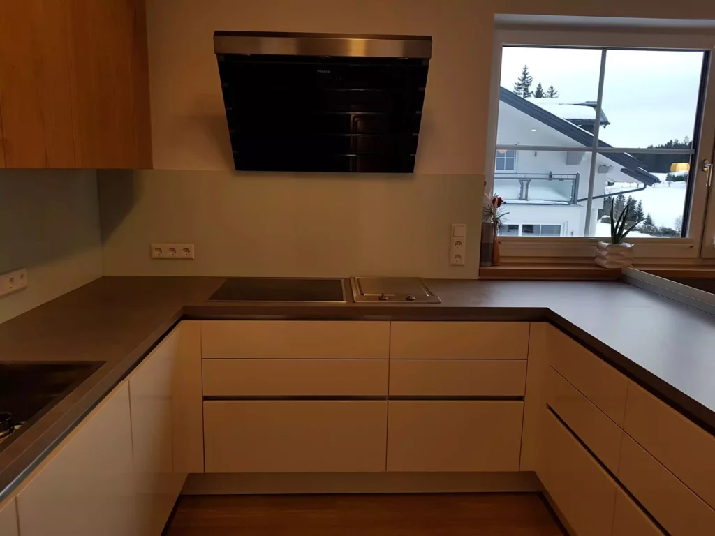 Moderne U-förmige Küche mit weißen Fronten, dunkler Arbeitsplatte, Kochfeld, Dunstabzug und großem Fenster mit, Referenzen