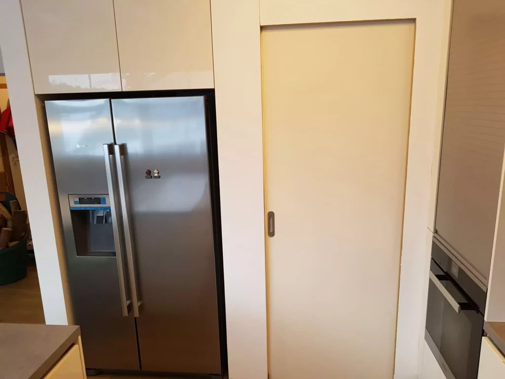 Küchenbereich mit eingebautem Edelstahl-Kühlschrank, weißen Oberschränken, Schiebetür und Backofen als Teil einer, Referenzen