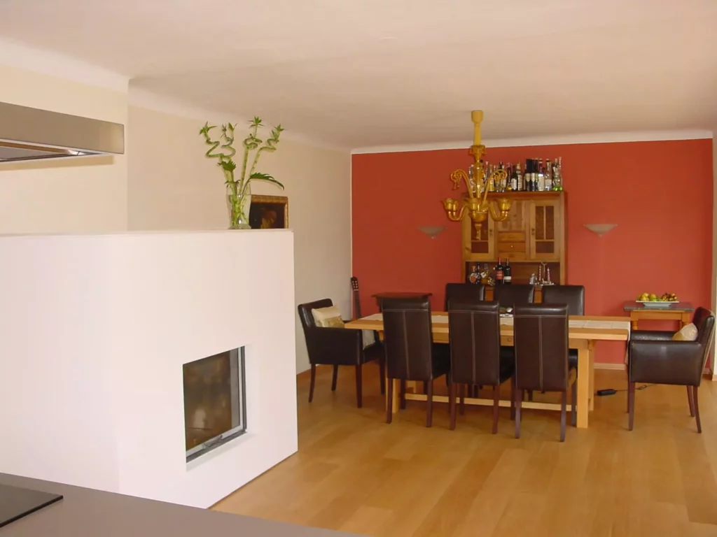 Esszimmer mit Holztisch, sechs dunkelbraunen Lederstühlen, Kamin und roter Akzentwand mit Holzschrank und, Referenzen