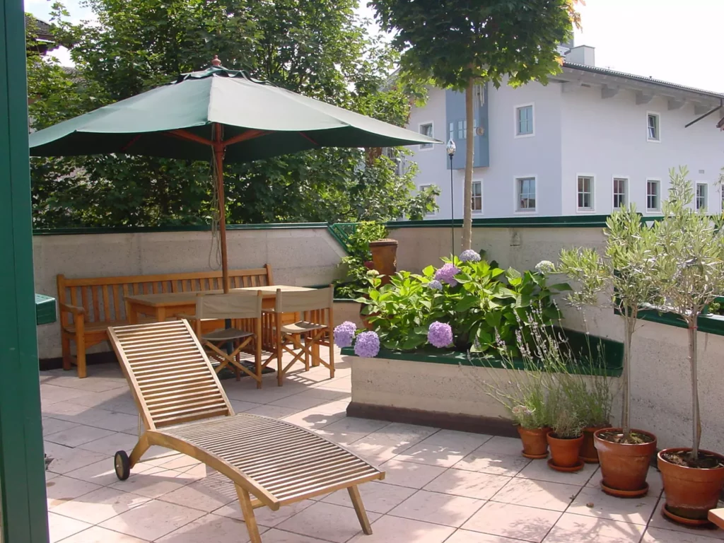 Terrassenbereich mit Poliform-Holzliegen, Gartentisch, Stühlen, grünem Sonnenschirm und bepflanzten Kübeln in, Referenzen