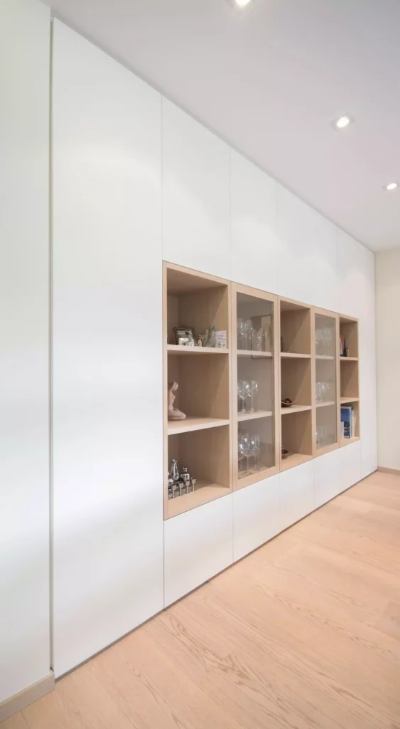 Maßgefertigte weiße Einbauwand mit offenen und verglasten Regalfächern aus hellem Holz in modernem Wohnraum, Referenzen