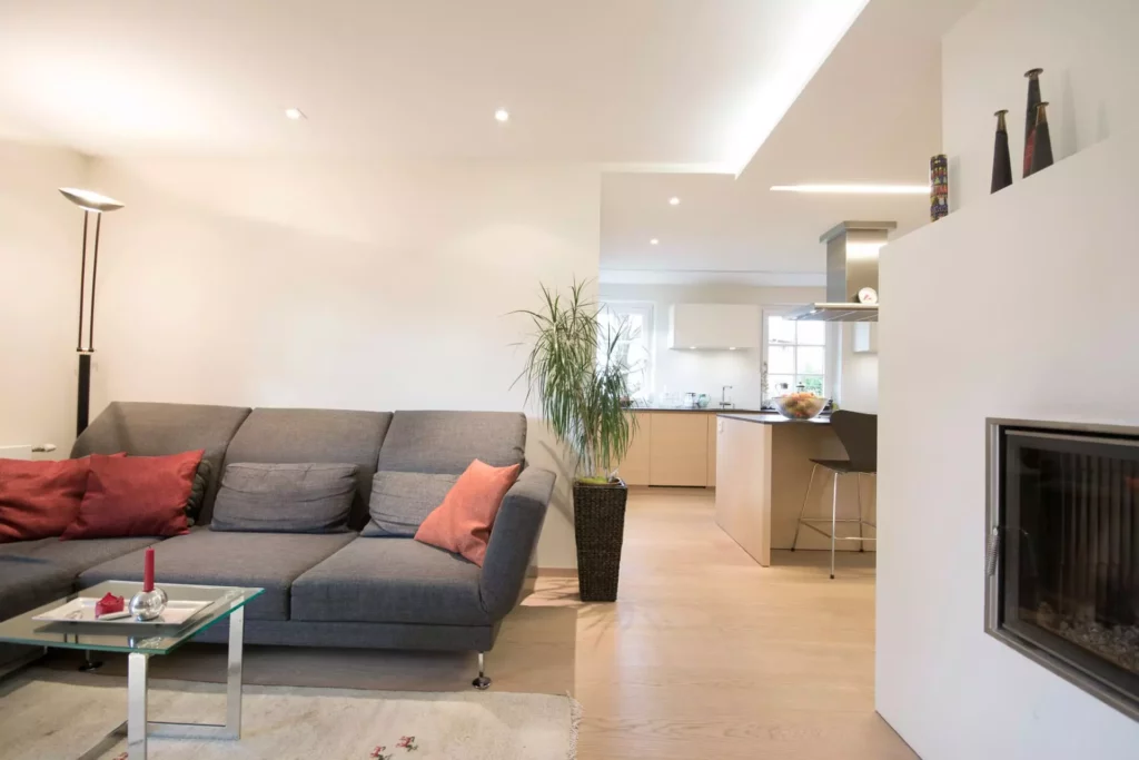 Moderner Wohnraum mit grauem Poliform Sofa, offener Küche mit Holzfronten, Kamin und Pflanze in hellem, Referenzen