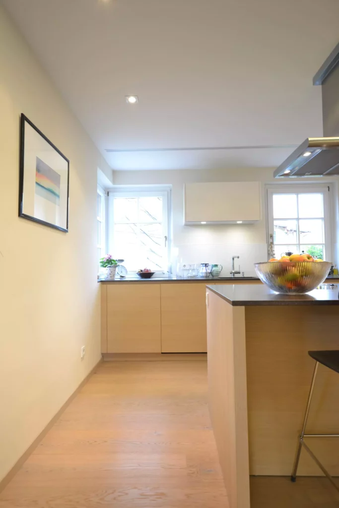 Moderne helle Küche mit Poliform-Möbeln, Holzfronten, Kücheninsel mit Obstschale und großem Fenster in Altenmarkt, Referenzen