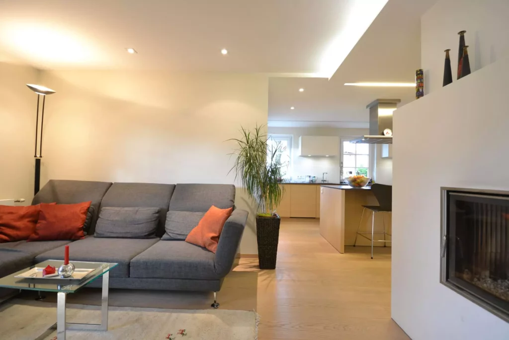 Moderner Wohnbereich mit grauem Poliform Sofa, orangen Kissen, Glas-Couchtisch, Pflanze und offener Küche mit, Referenzen