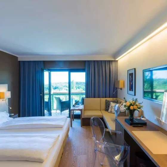 Modern eingerichtetes Hotelzimmer mit Doppelbett, Ecksofa, Schreibtisch mit transparentem Stuhl und Balkon mit, Referenzen