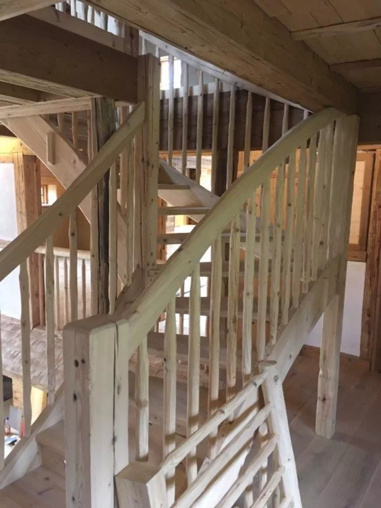 Massgefertigte Holztreppe mit handwerklich bearbeitetem Geländer in einem Innenraum mit sichtbaren Holzbalken, Referenzen
