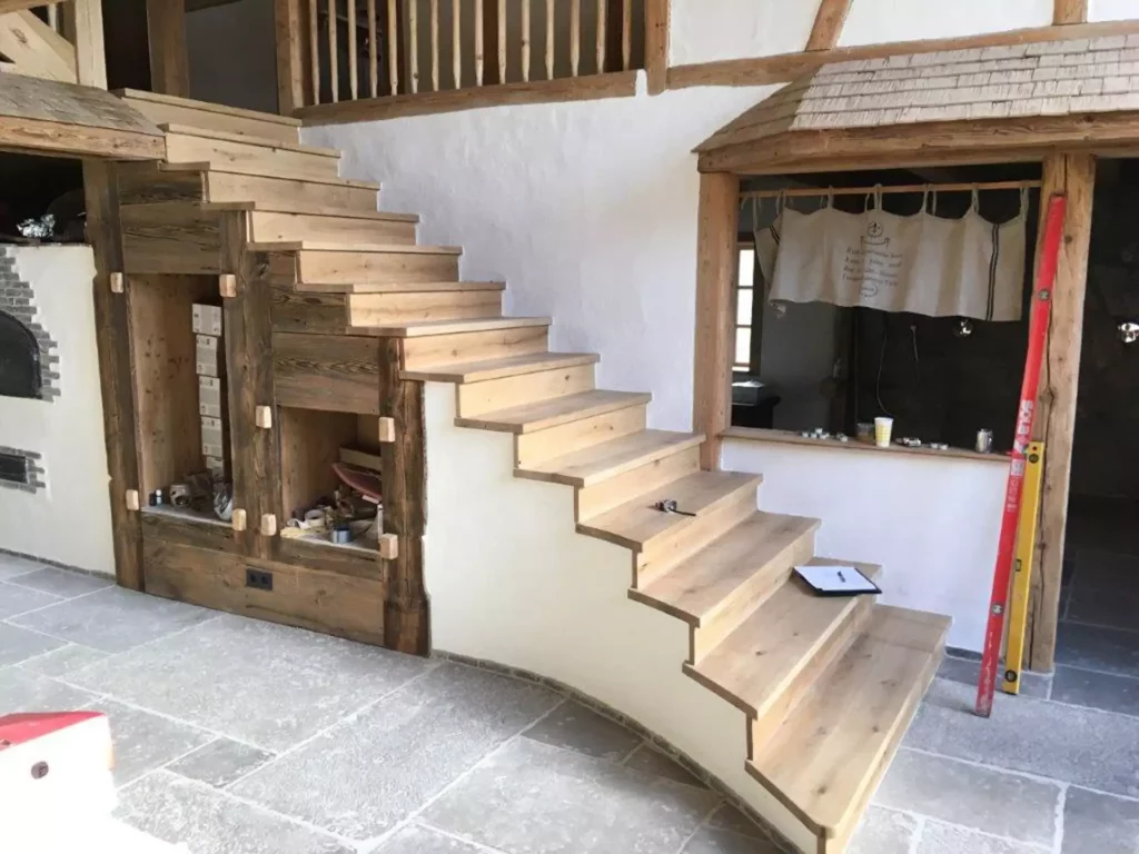 Massgefertigte Holztreppe mit rustikalem Design und integrierten Regalfächern in einem Innenraum mit Steinboden, Referenzen