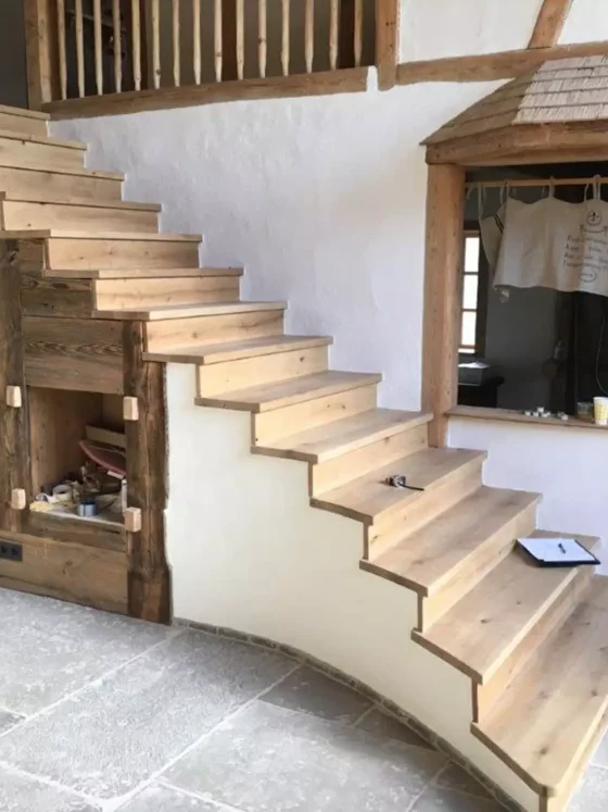 Massgefertigte Holztreppe mit rustikalem Design und integrierten Regalfächern in einem Innenraum mit Steinboden, Referenzen
