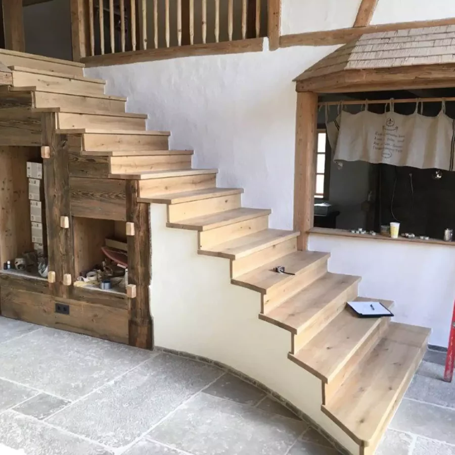 Massgefertigte Holztreppe mit rustikalem Design und integrierten Regalfächern in einem Innenraum mit Steinboden, Referenzen