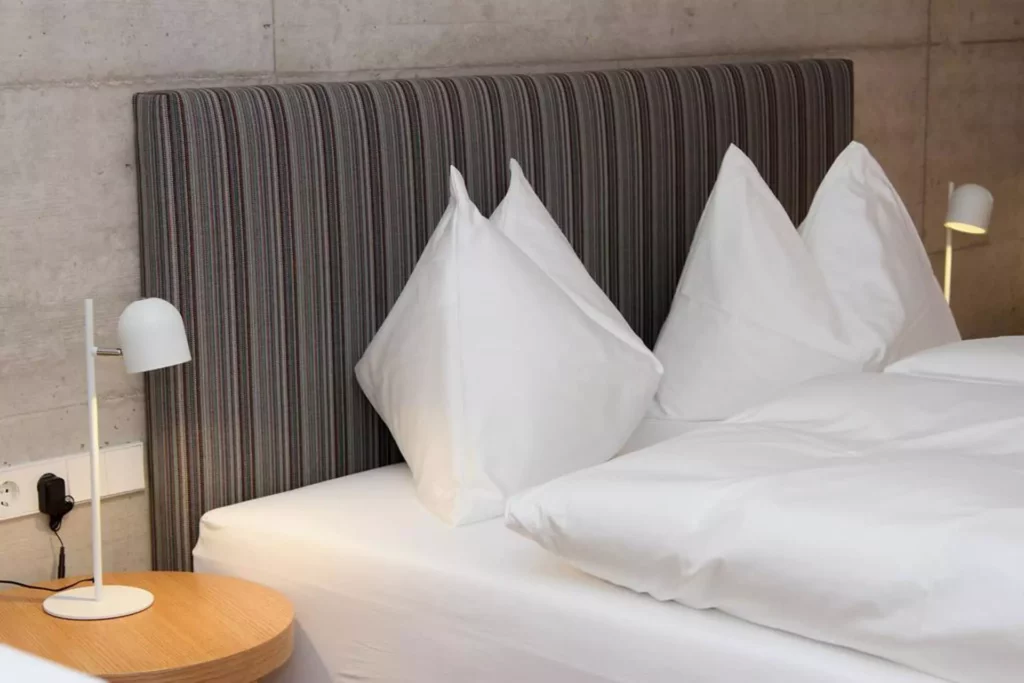 Modernes Schlafzimmer mit gestreiftem Polsterkopfteil, weißen Kissen, Bettwäsche und zwei weißen, Referenzen